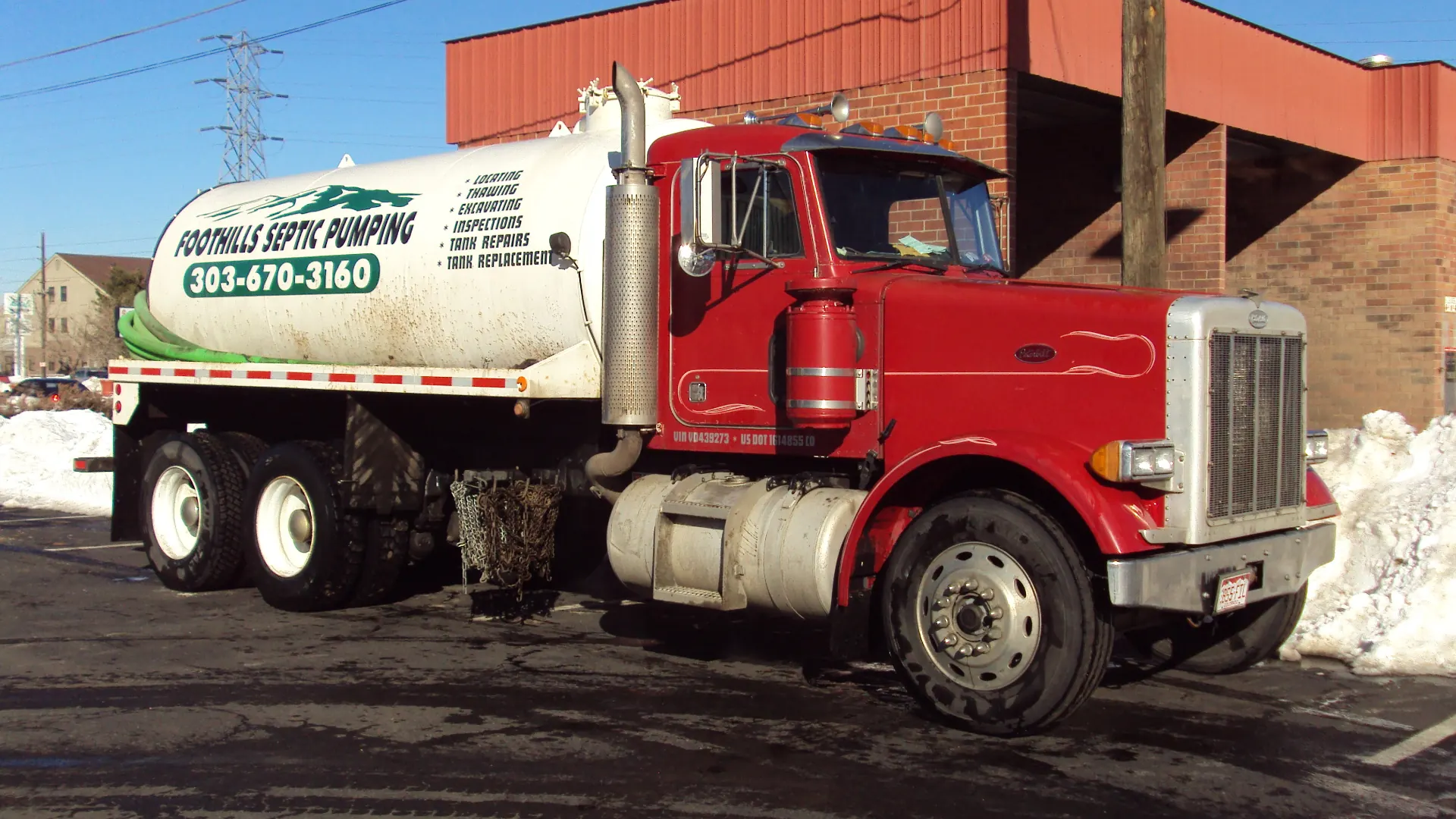 Foothills Septic Pumping's red Peterbilt pump truck with its white tank, parked in the snow