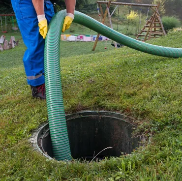 Pump hose running into an open septic tank riser on a lawn