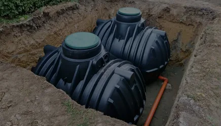Two black septic tanks set side by side in a fresh excavation